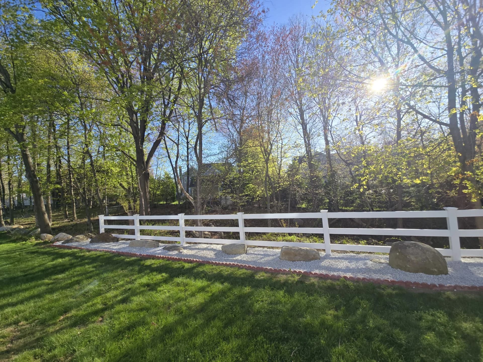 White three-rail fence along the wooded edge of a yard in Shrewsbury, MA