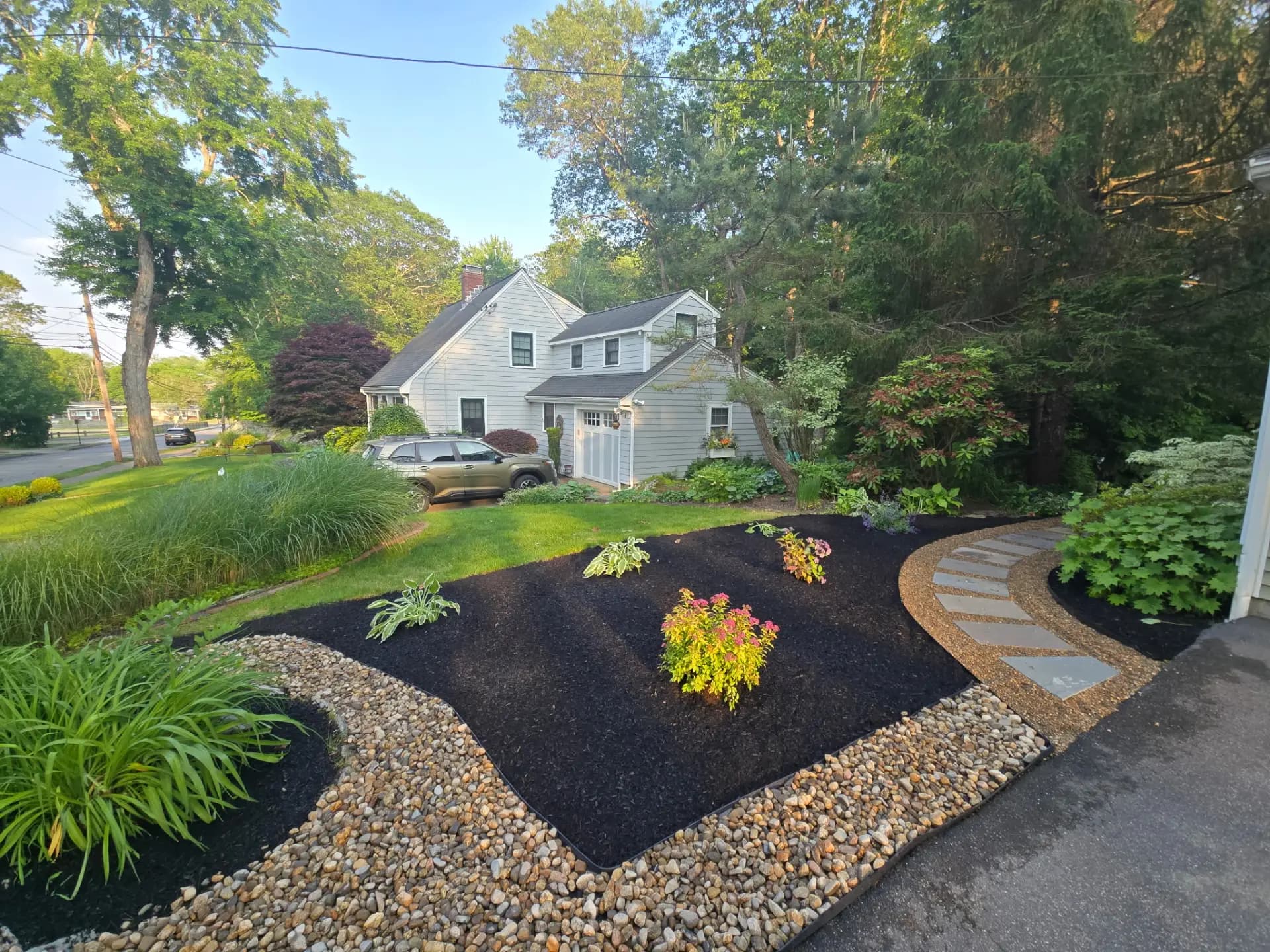 Landscaped front yard with a green lawn, mulched planting beds and a river-stone border